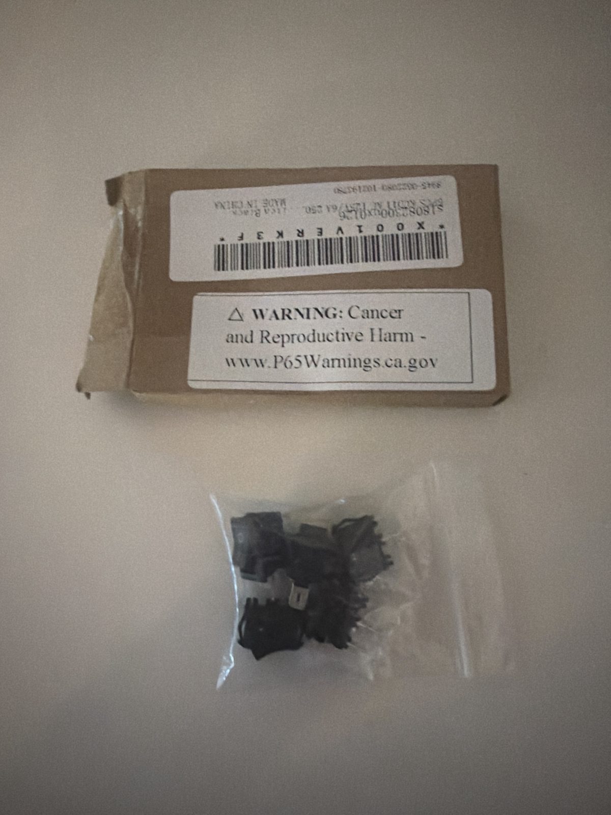 A small cardboard box with a barcode label, and below it a clear bag holding five black mini rocker switches